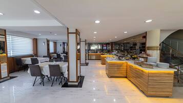 Un moderno hall de hotel con zona de comedor, mostrador de recepción y una escalera.