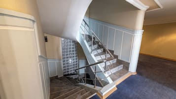 Una escalera con barandilla de vidrio, una pared azul y piso alfombrado.
