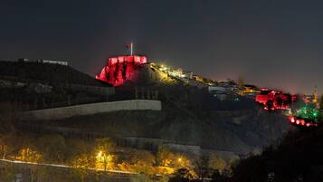 Una estructura fortificada con una bandera en la parte superior, rodeada por un paisaje montañoso con senderos iluminados y edificios.