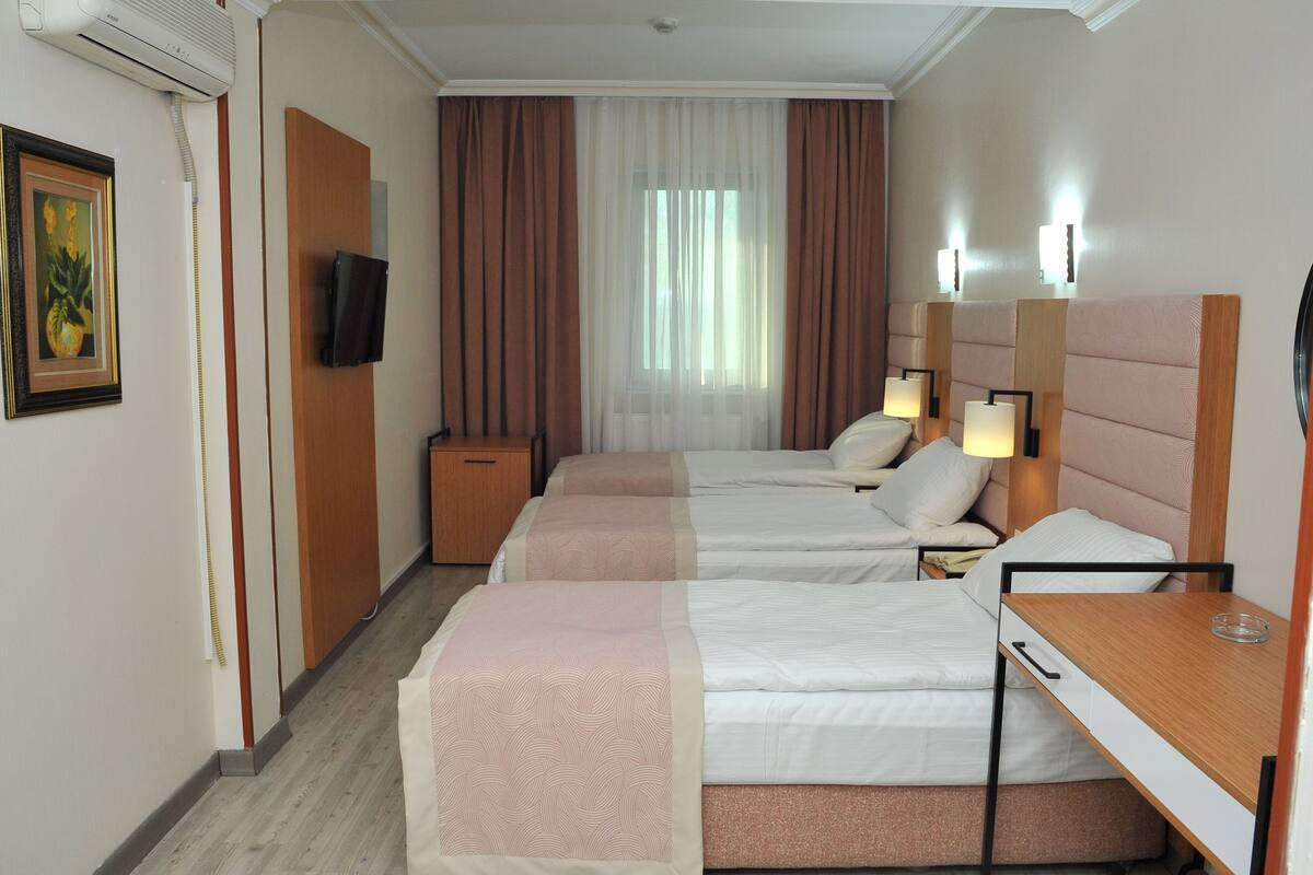 A hotel room with two beds, a desk, a TV, and a window with curtains.