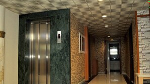 A hallway with a marble elevator, a stone wall, and a wooden bench. - Lion City Hotel Ankara (Ankara)