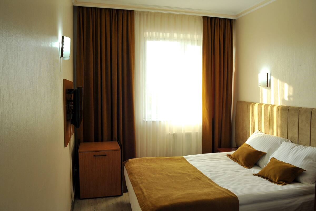 A hotel room with a bed, a nightstand, a television, and a window with curtains.