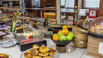 Un bufé con diversas opciones de comida, incluyendo carnes frías, quesos, frutas y pasteles.