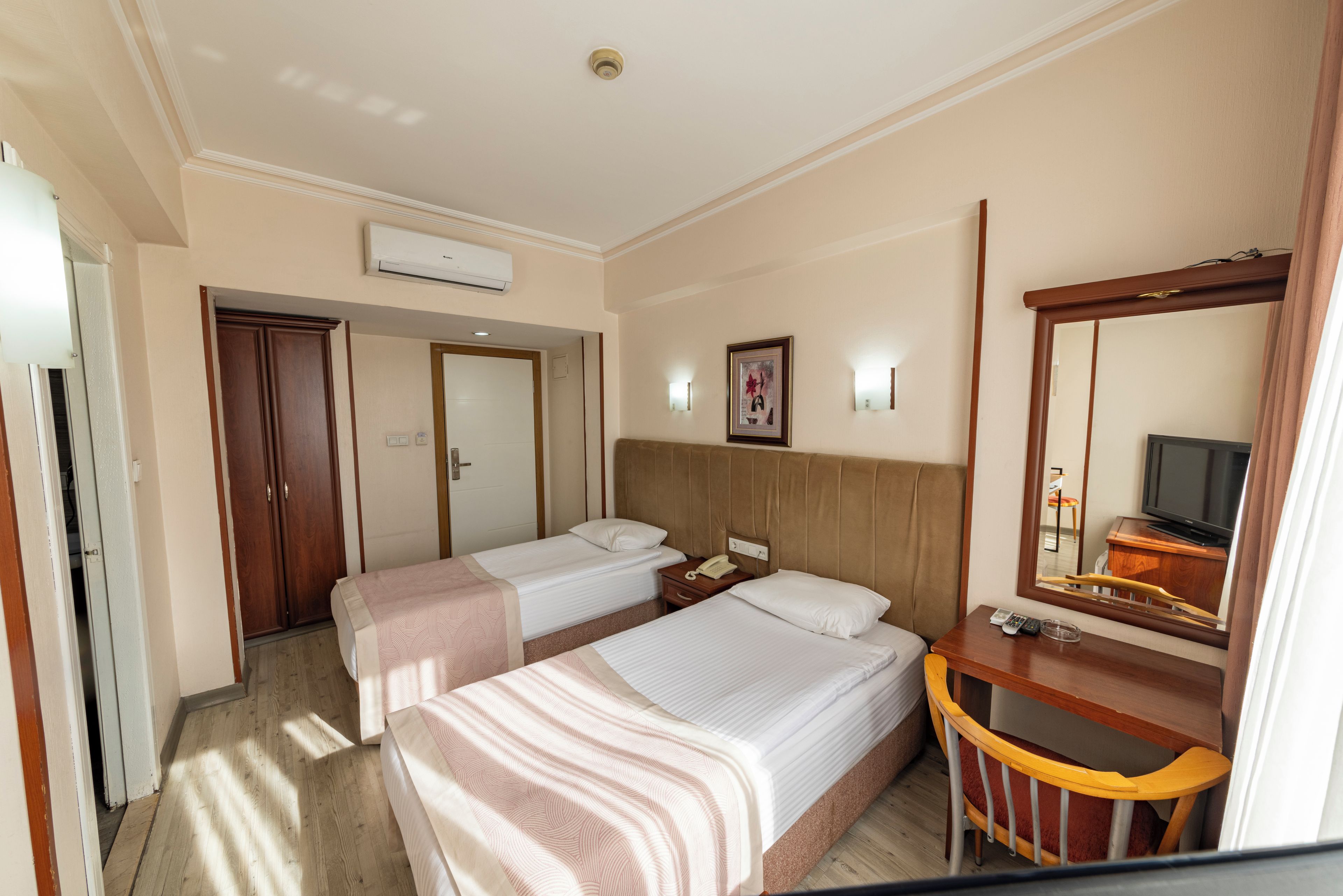 A hotel room with two beds, a desk with a chair, a mirror, and a television.
