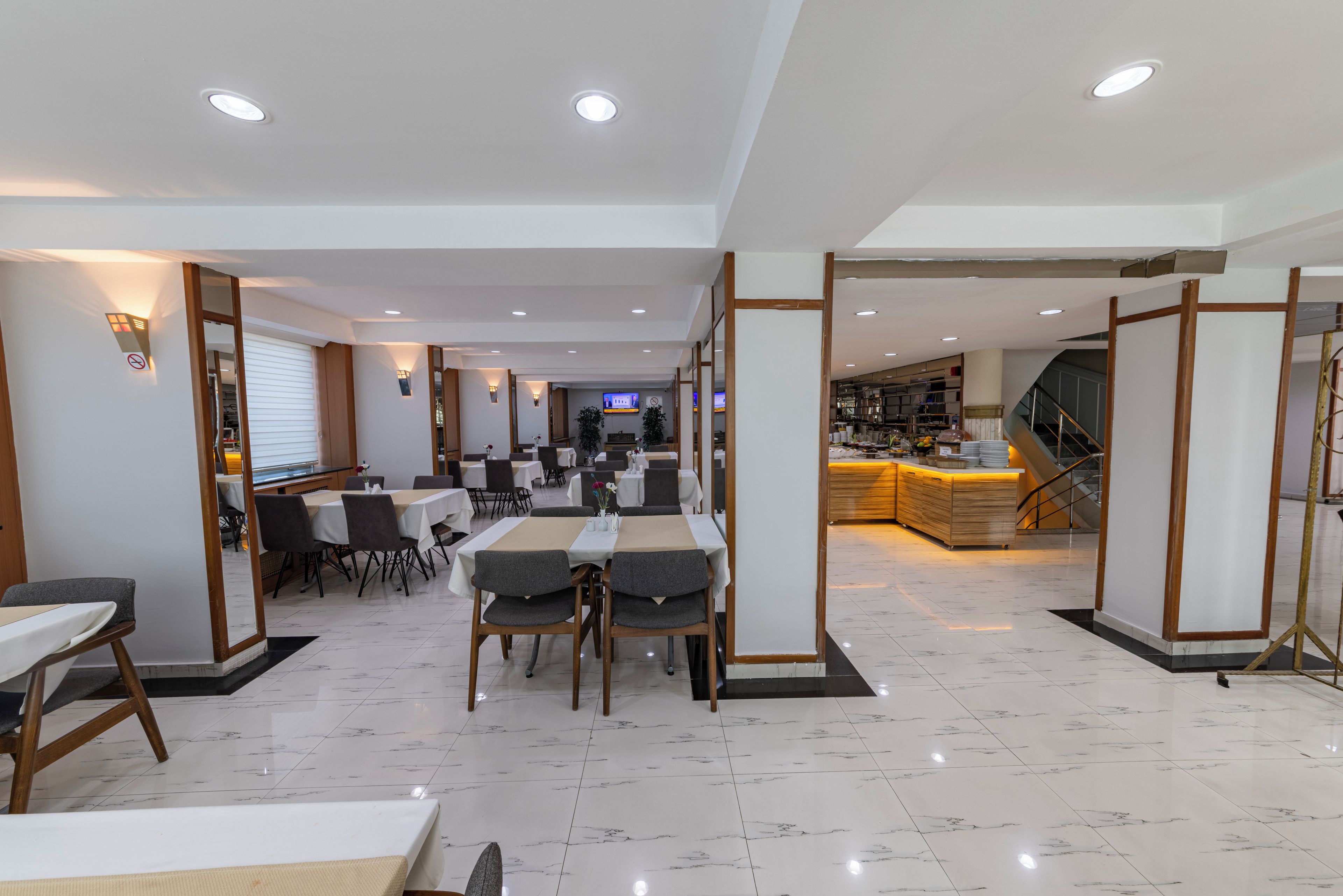 A hotel dining area with tables and chairs, a reception desk, and a kitchen in the background.