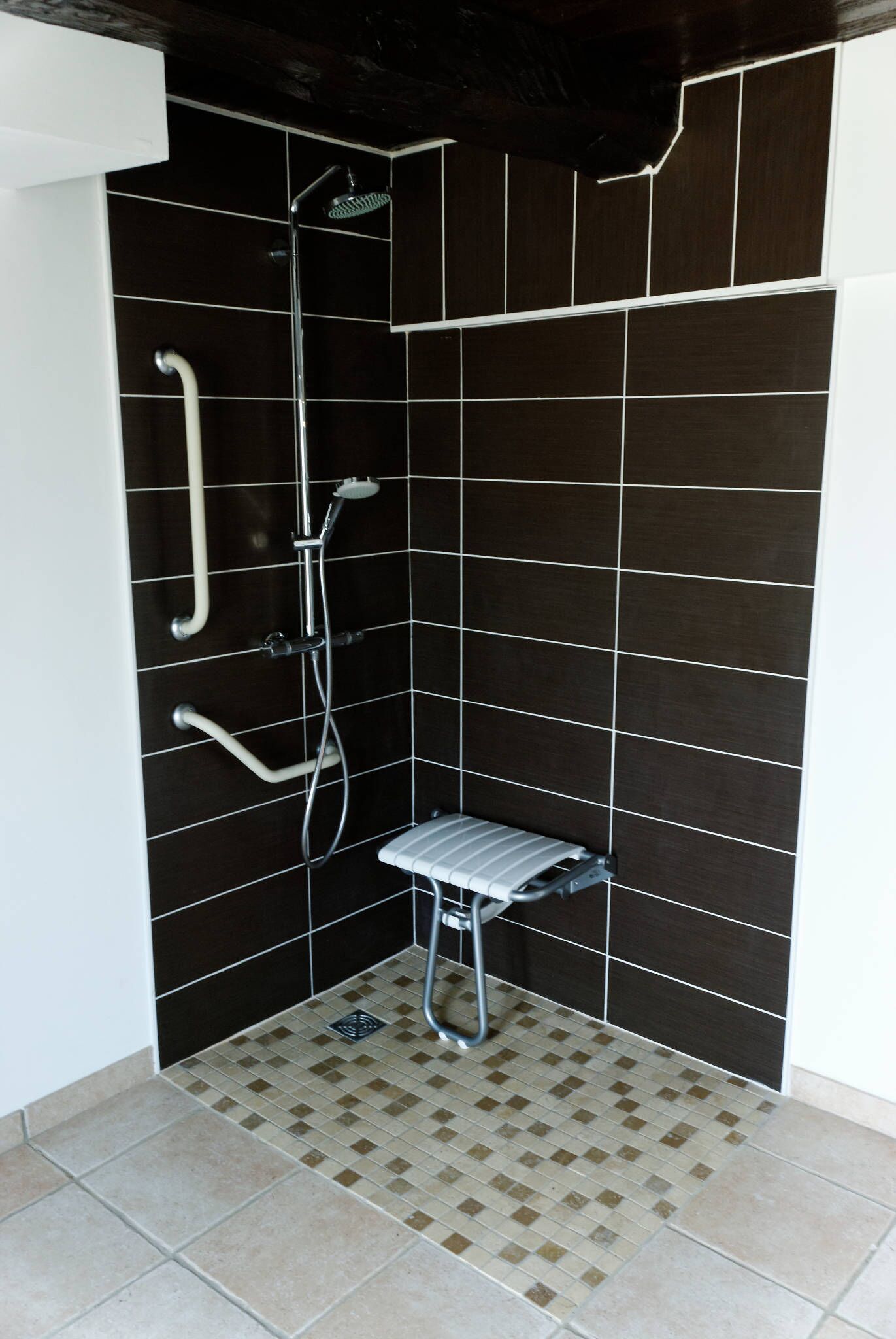A small, tiled shower area with a handheld showerhead, a wall-mounted faucet, and a shower seat.