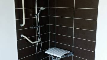 A small, tiled shower area with a handheld showerhead, a wall-mounted faucet, and a shower seat.