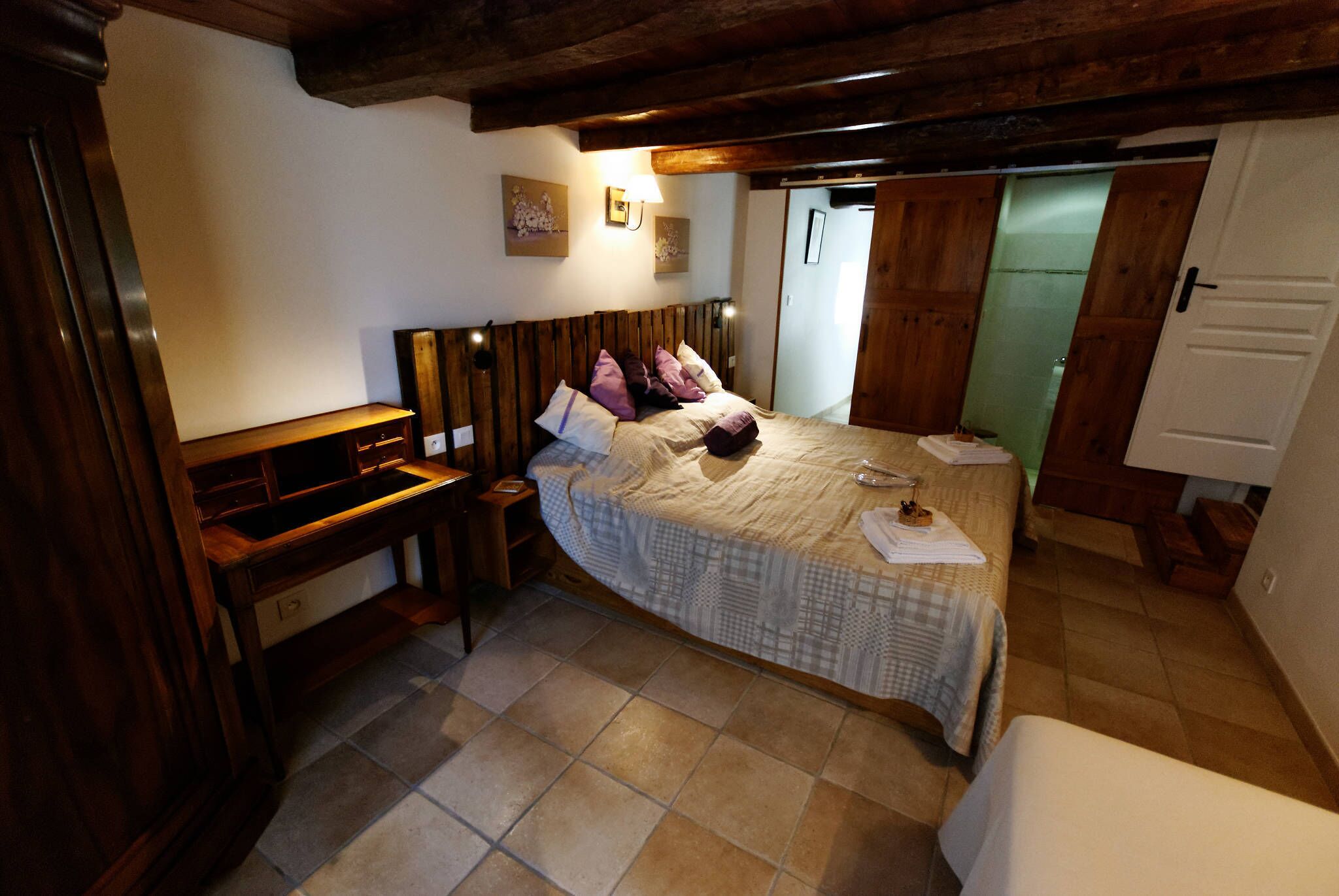 Un dormitorio con cabecera de madera, cama con colcha a cuadros, mesita de noche y velador.