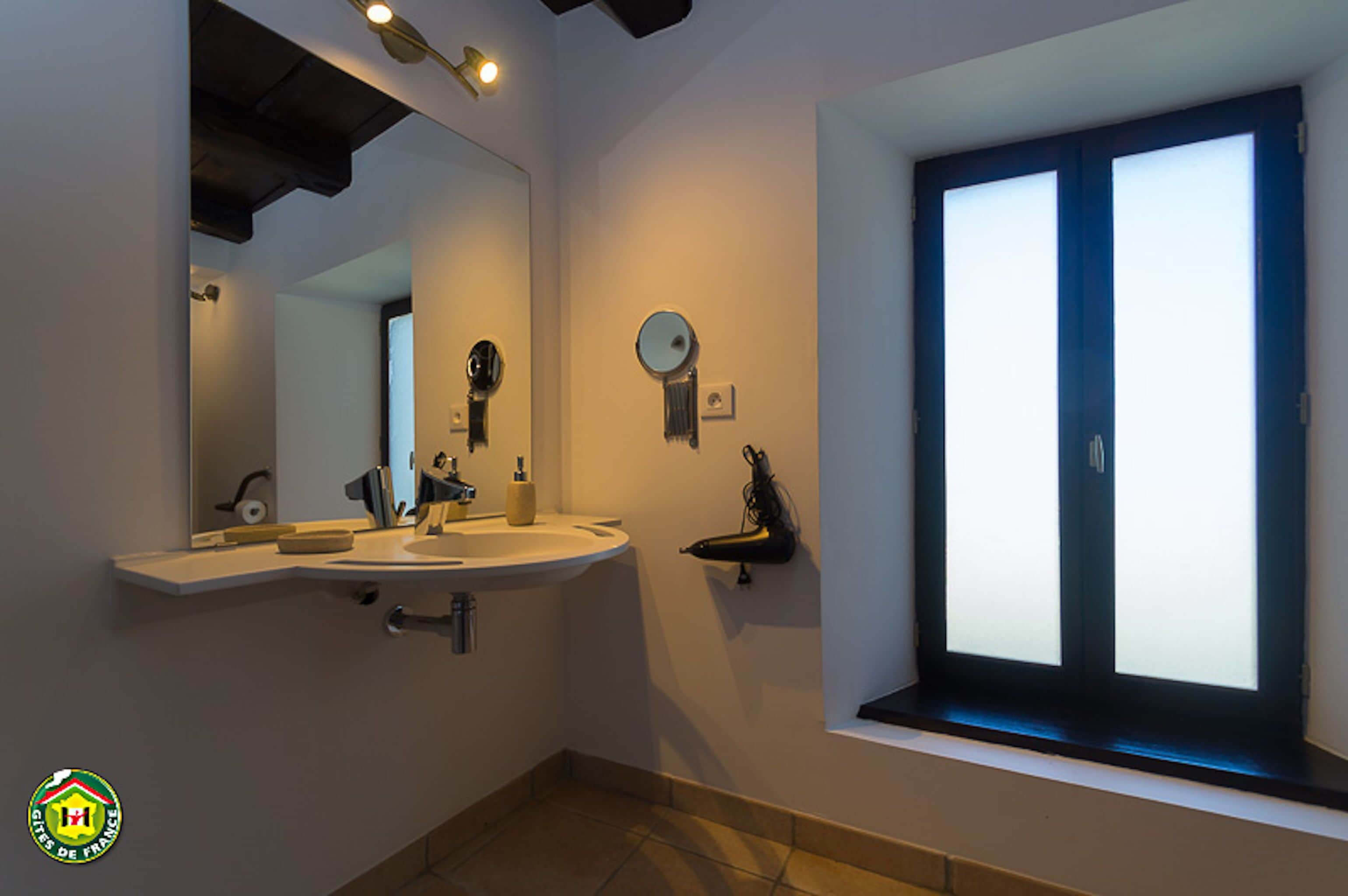 A bathroom with a large mirror, a sink, and a window with frosted glass.