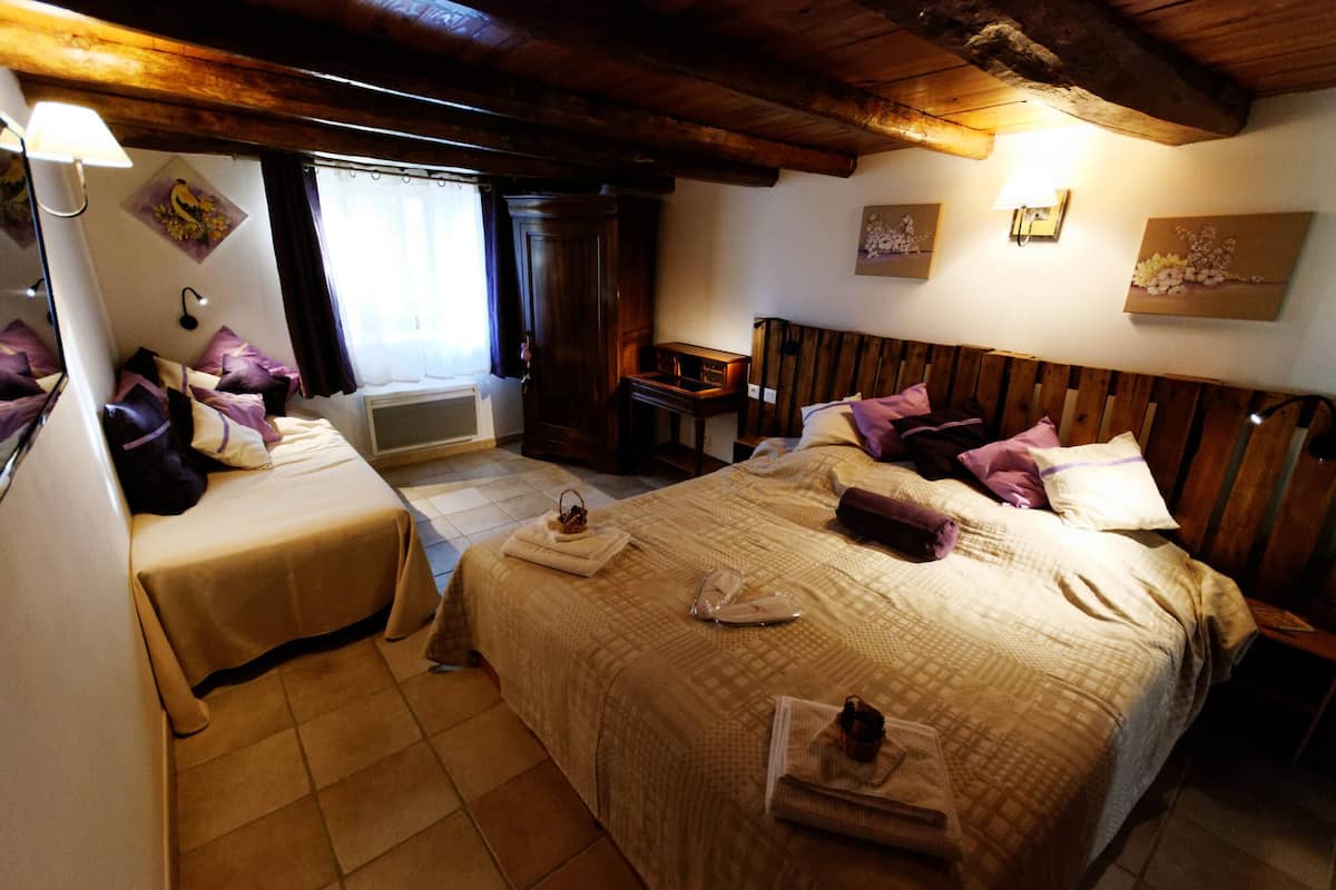 Quarto de hotel com duas camas, teto de madeira, uma mesinha e uma luminária fixada na parede.