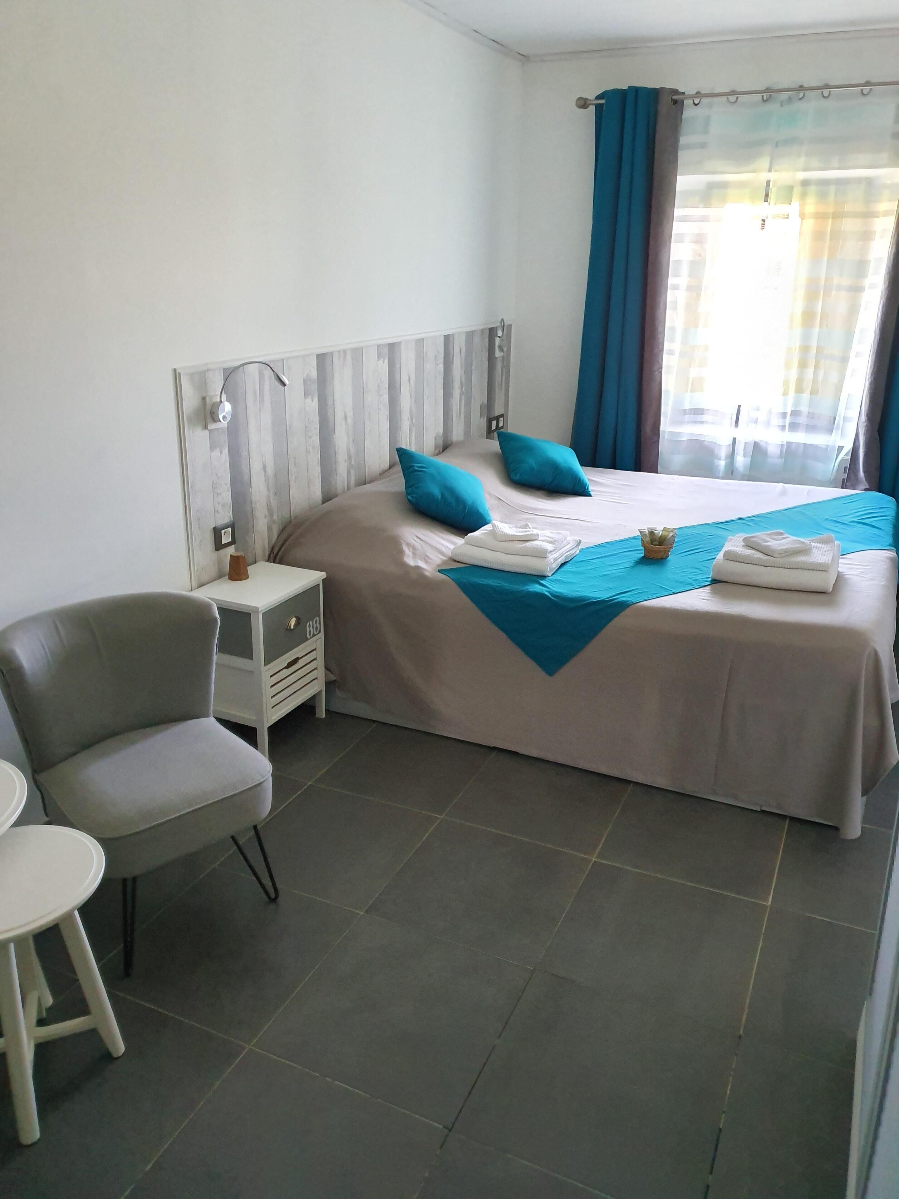 Habitación de hotel con cama, una silla, una mesita de noche y una ventana con cortinas.