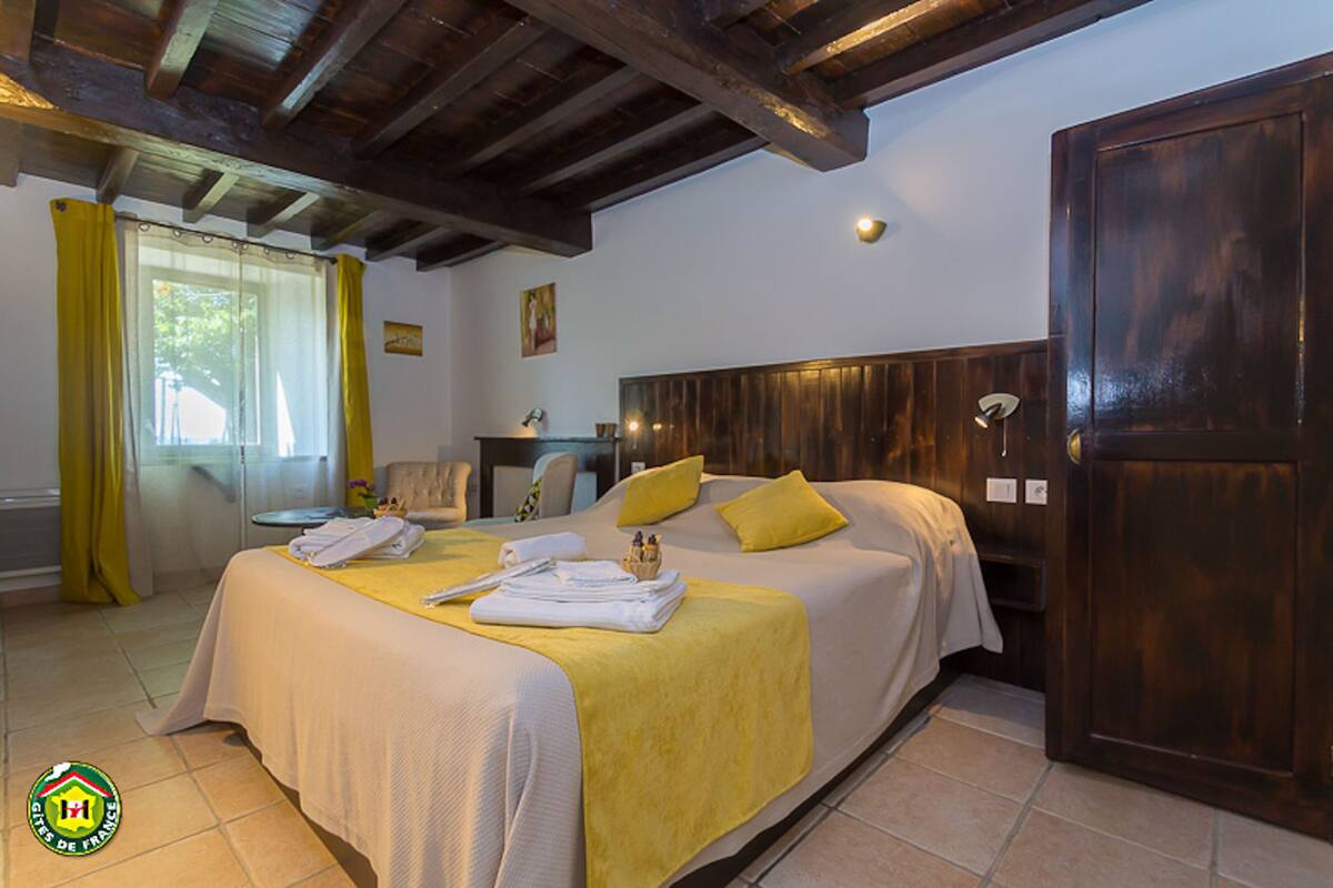 Quarto de hotel com duas camas, cabeceira de madeira, roupa de cama amarela, uma porta de madeira e uma janela com cortinas amarelas.