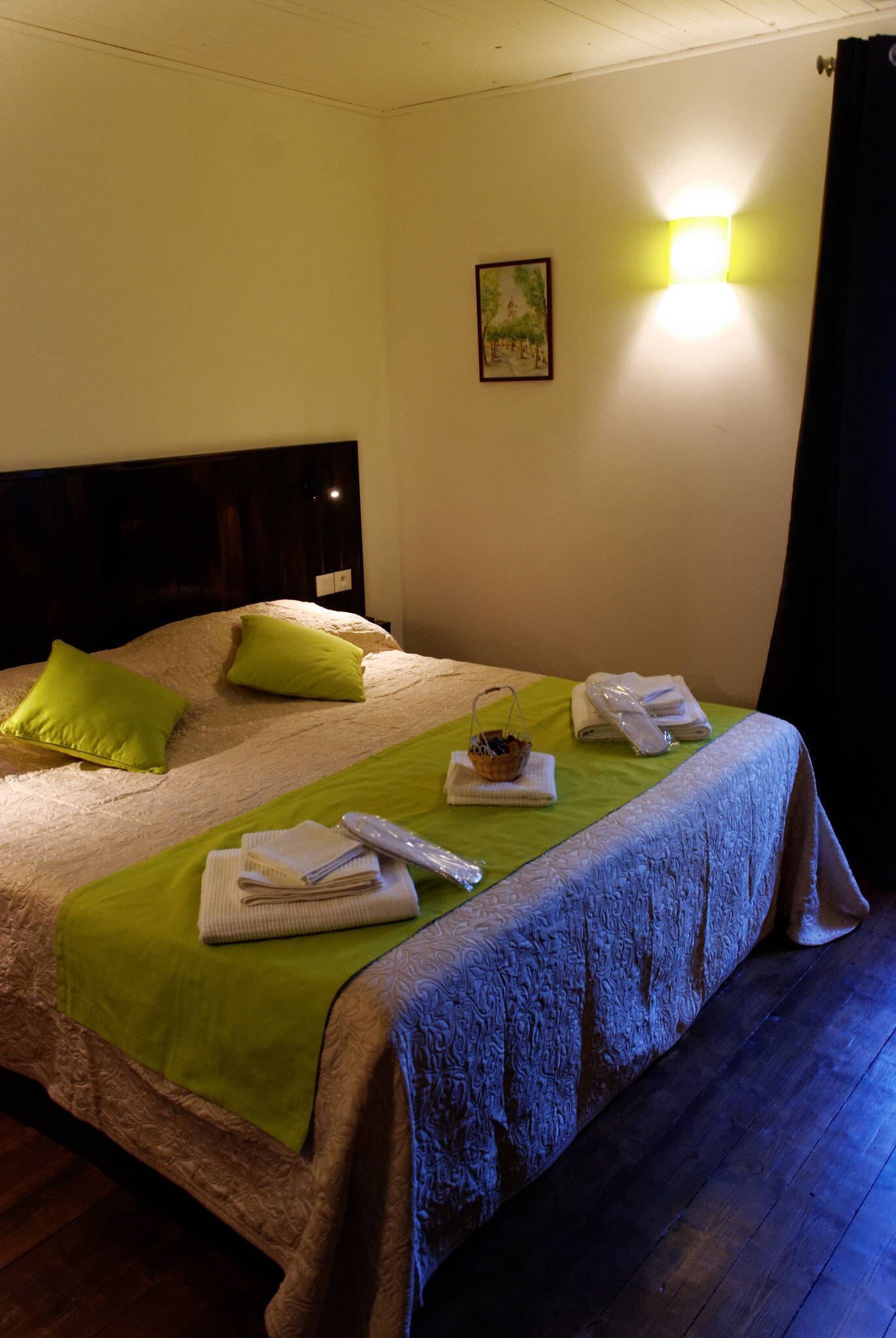 A neatly made bed with green pillows, a basket, towels, and a remote control on a green bedspread.