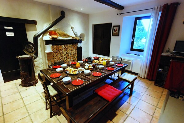 Un comedor con una mesa larga dispuesta para una comida, una chimenea y un ventanal con cortinas.