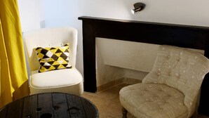 Una habitación con un sillón blanco, una mesa negra, una cortina amarilla y un cuadro en la pared.