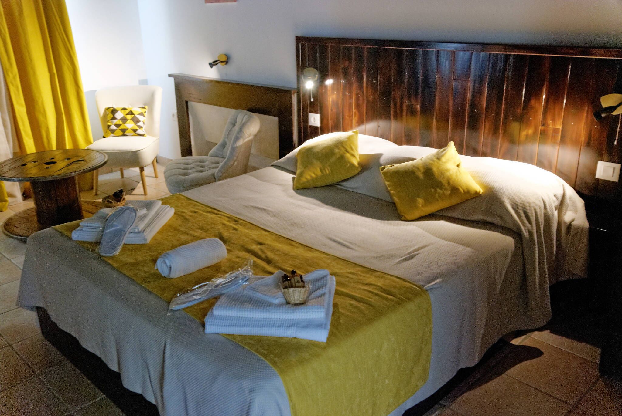 A hotel room with a large bed, a round table, a chair, and a bedside table.