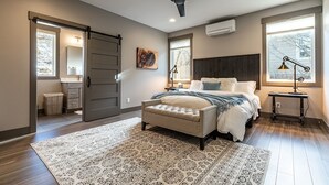 A bedroom with a bed, a ceiling fan, a large window, and a door leading to another room.