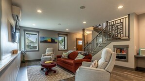 A spacious living room with a fireplace, a staircase, and a large window.