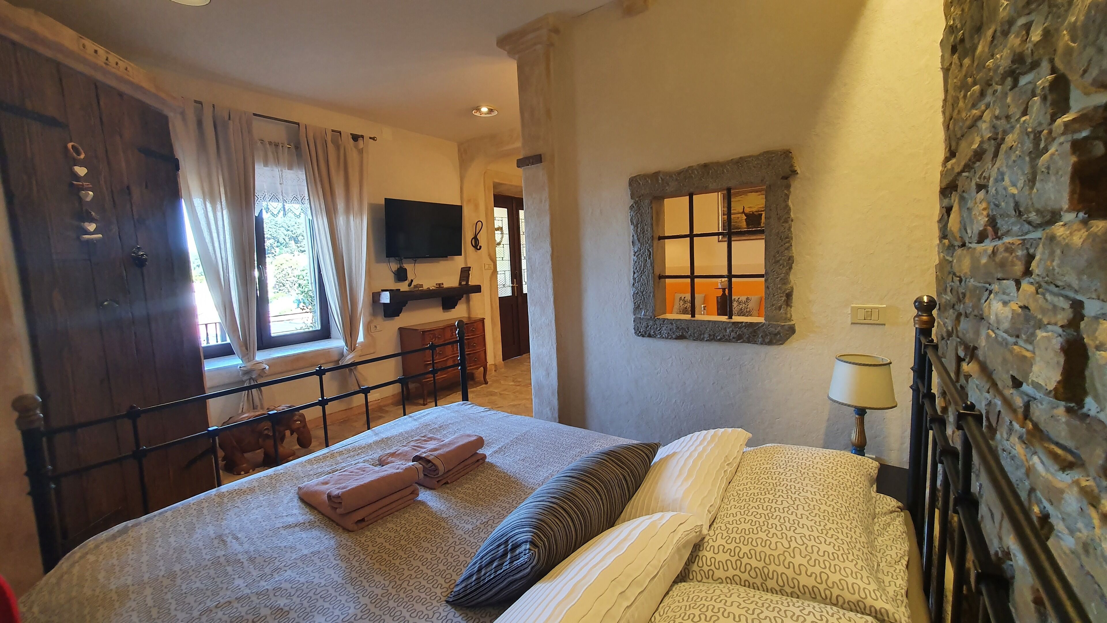 A bedroom with a bed, a TV, a stone wall, and a window with curtains.