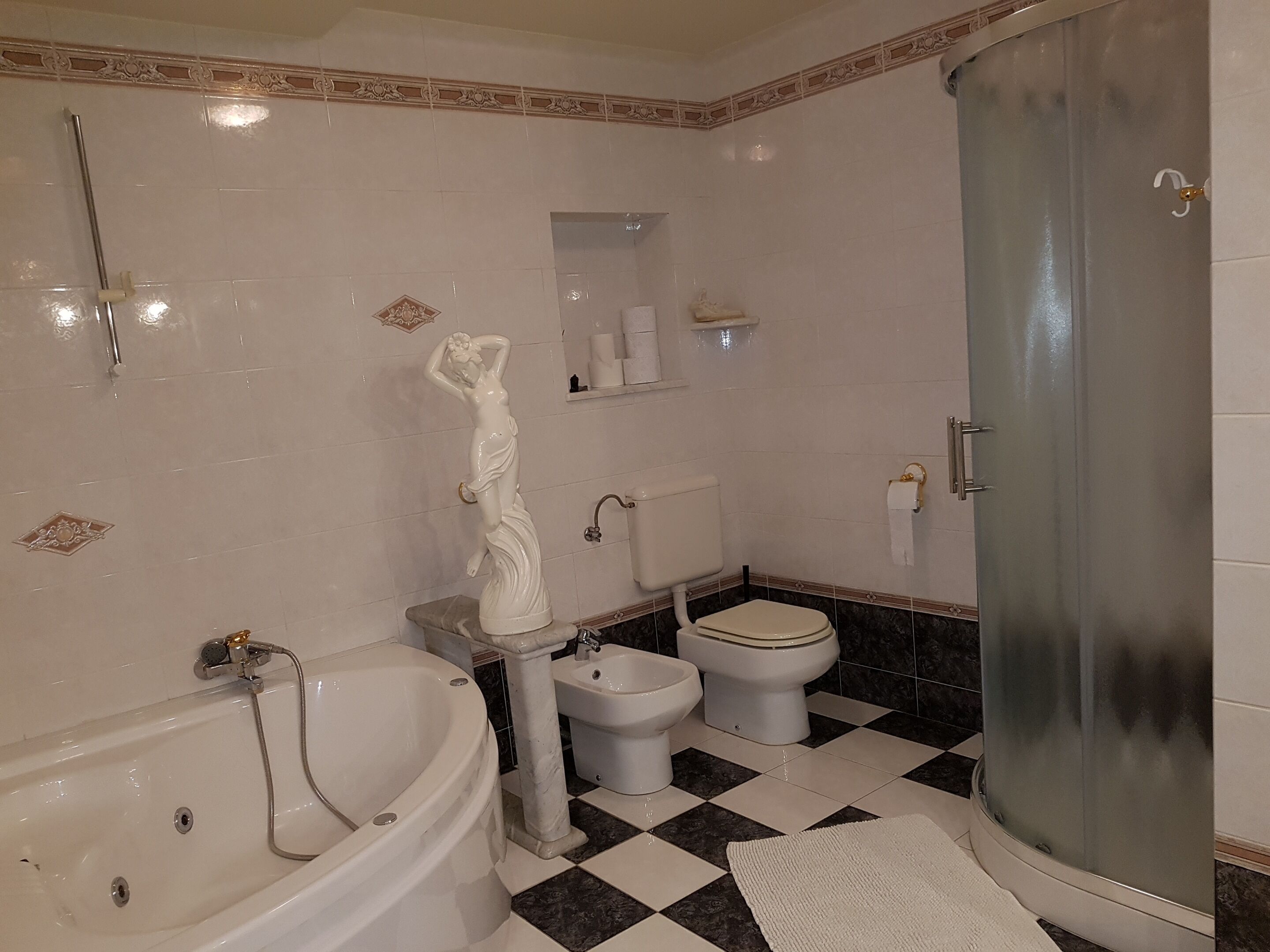 Une salle de bain avec une baignoire, une douche, deux toilettes, un sol en marbre et une statue décorative.
