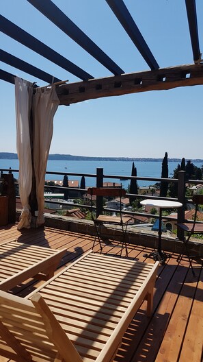 A wooden deck with a pergola, a table, and chairs overlooking a body of water.