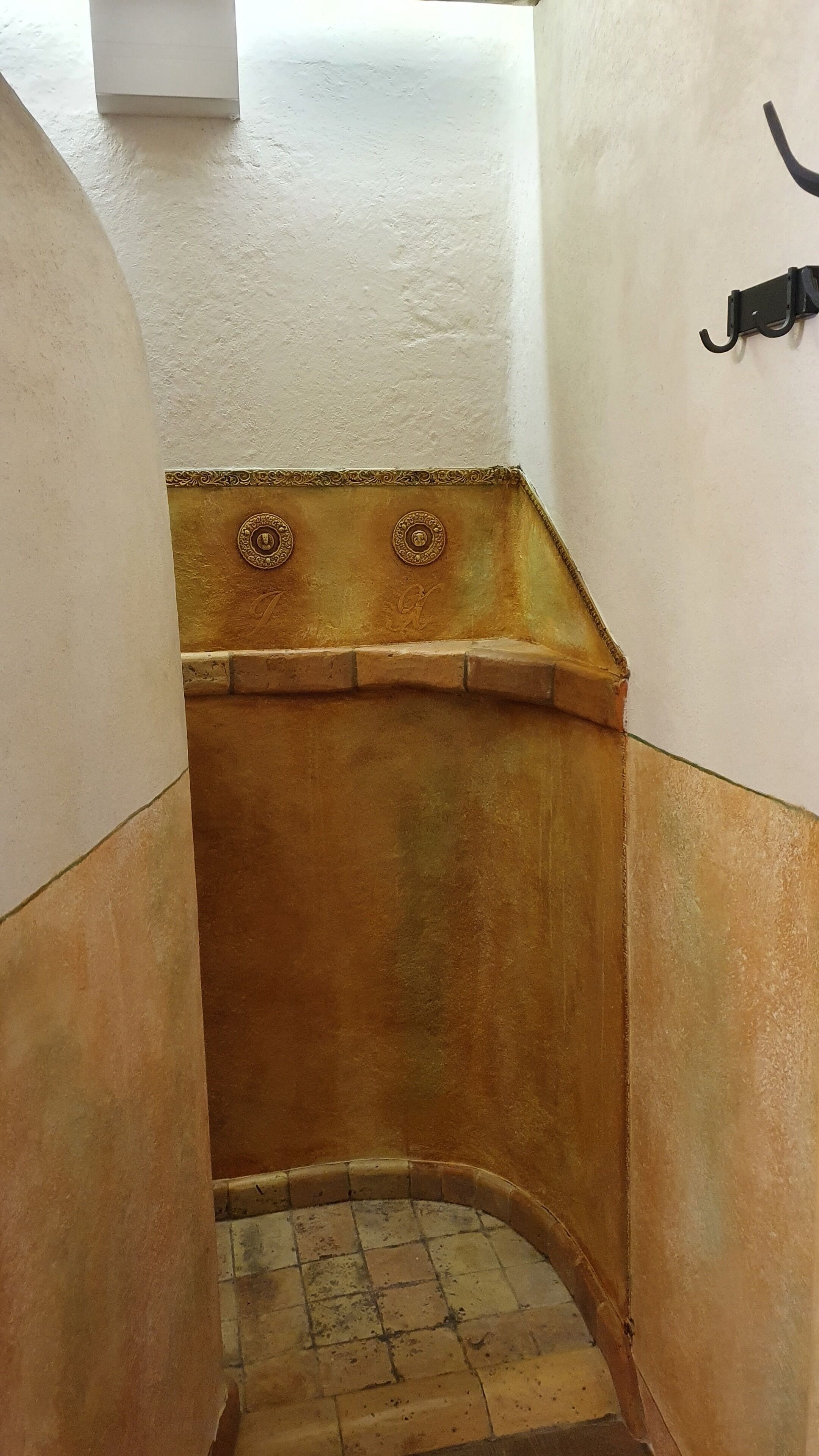 A narrow, enclosed stairwell with a tiled floor and a decorative, rust-colored wall.