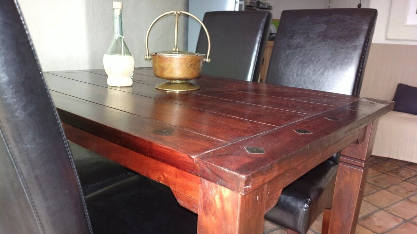 Una mesa de madera con sillas, una botella y un recipiente metálico encima.
