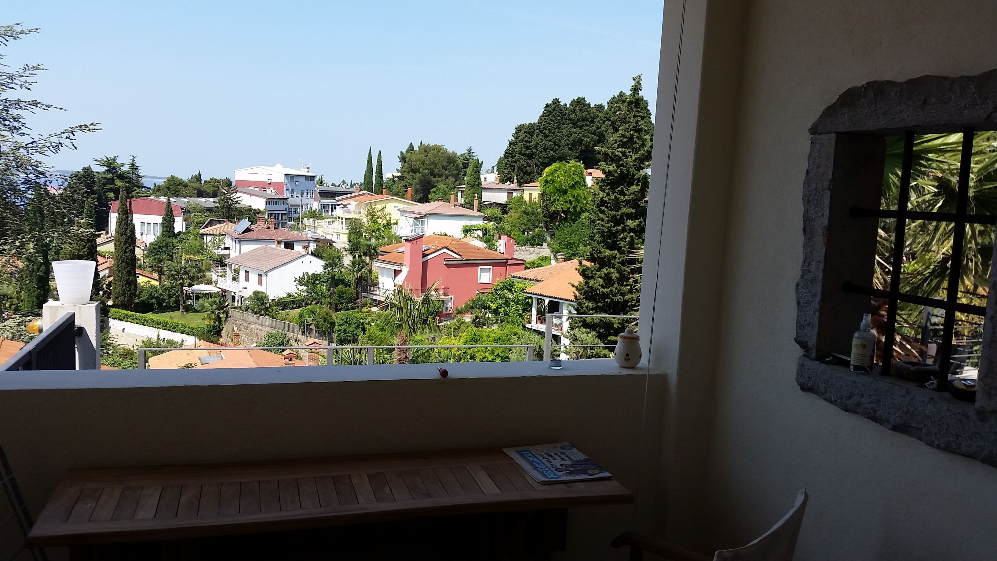 Un balcon donnant sur un quartier résidentiel, une table en bois et une fenêtre offrant une vue sur des maisons et des arbres.