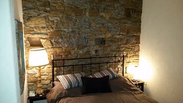 Cama com parede de pedra ao fundo, duas luminárias de cabeceira e um travesseiro listrado.