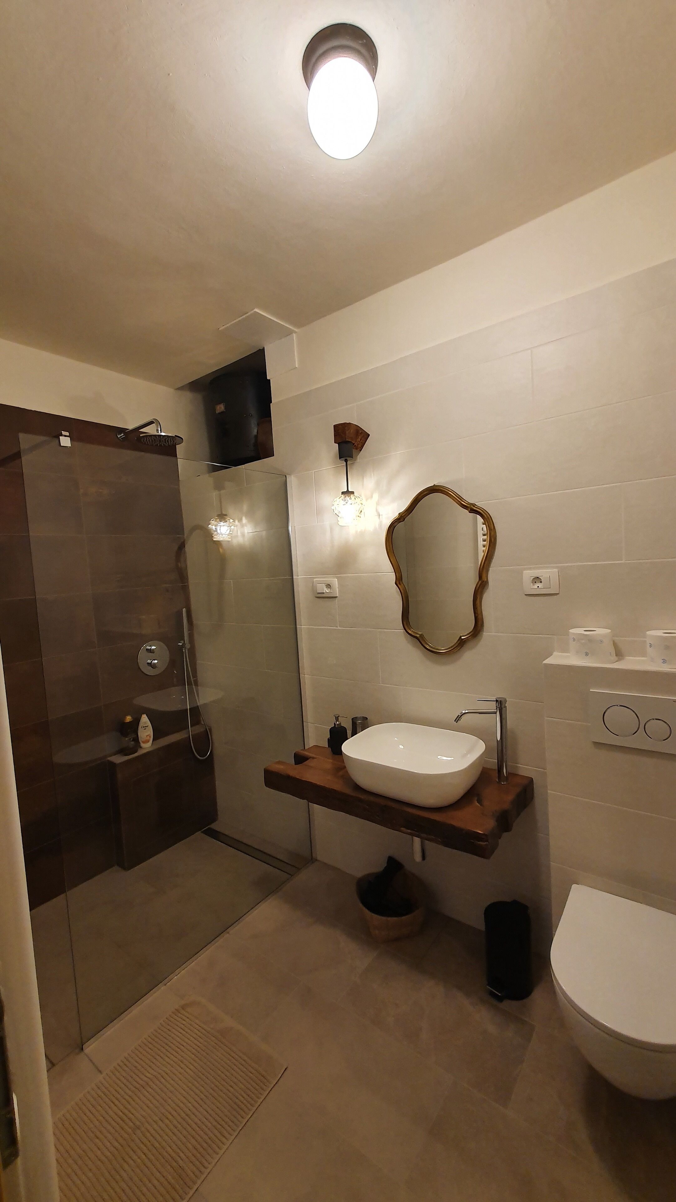 Un baño moderno con ducha envuelta en cristal, tocador de madera con lavamanos blanco, espejo y retrete.