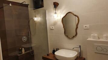 Un baño moderno con ducha envuelta en cristal, tocador de madera con lavamanos blanco, espejo y retrete.