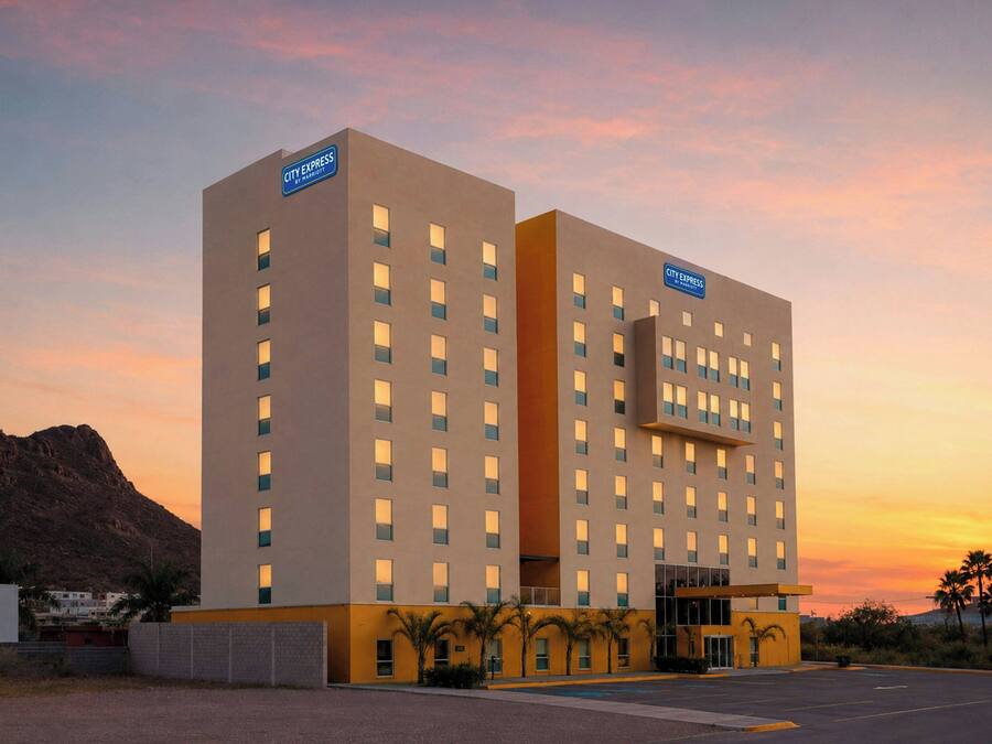 A City Express hotel with a modern design, featuring a prominent entrance, multiple floors, and a parking lot.