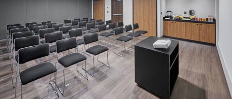 A conference room with rows of chairs, a podium, and a kitchenette area with food and beverages.