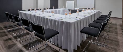 A conference room with a long table, black chairs, water bottles, and a projector screen.