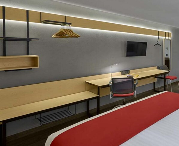 Habitación de hotel con una cama grande, un escritorio, una silla, un televisor y un armario con perchero.