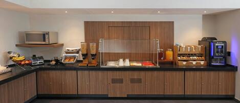 A modern kitchen with a microwave, coffee machine, and various food items on the counter.