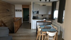 A modern kitchen with a dining area, wooden flooring, and a view of a green room. - Fantastic vacation apartment "Waldhonig" (St. Englmar)