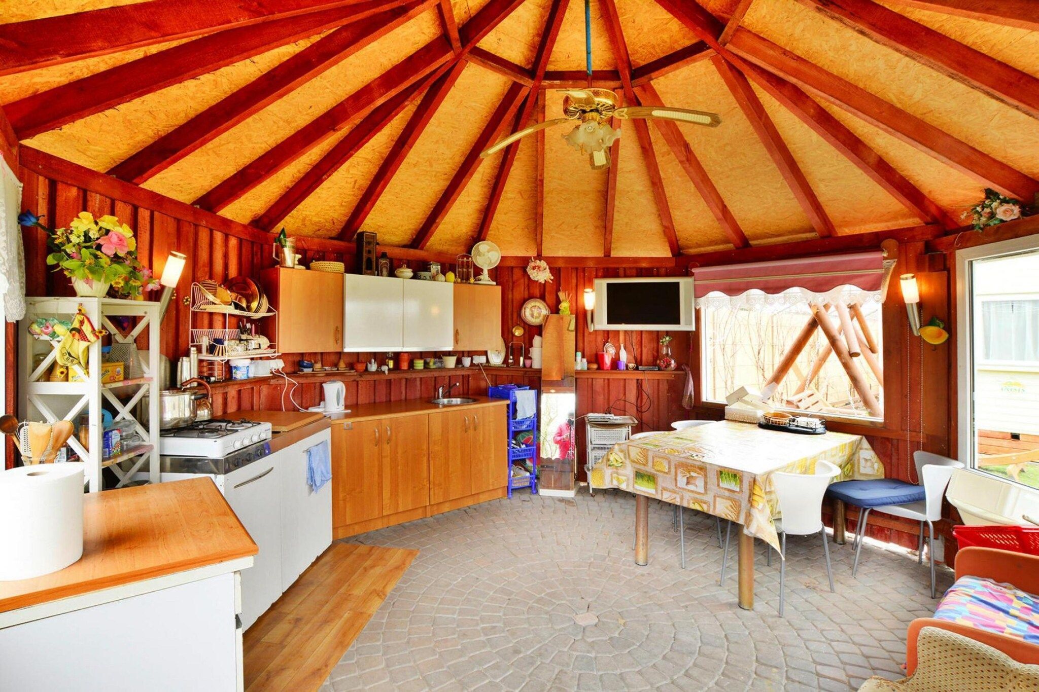 Un interior acogedor con techo de madera, una zona de cocina, una mesa de comedor y un televisor montado en la pared.