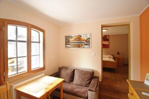 A room with a wooden table, a brown sofa, a painting of a car, and a bed in the background. - Apartment only 20 m from  Lake in Rekowo (Rekowo)