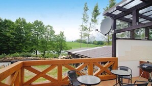 An outdoor patio with a wooden deck, metal chairs, a round table, and a barbecue grill. - Apartment only 20 m from  Lake in Rekowo (Rekowo)