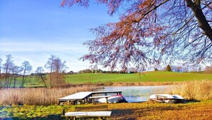 A lakeside picnic area with benches and tables, surrounded by trees and a grassy field.