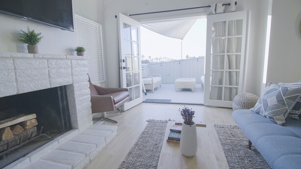 Una sala de estar con chimenea, un sofá, una mesa de centro y vistas al exterior a través de puertas abiertas.