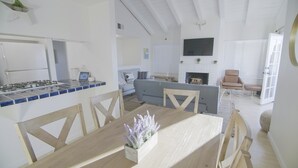 Una cocina moderna con estufa a gas, una mesa de comedor con sillas y un área de estar con sofá y televisor.