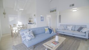 Una sala de estar moderna con un sofá azul claro, un sillón a juego y una mesa de centro con libros. Hay un comedor con una mesa y sillas de madera.