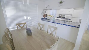 Un comedor con mesa y sillas de madera, una planta en maceta y una cocina con armarios blancos y salpicadero de azulejos azules.