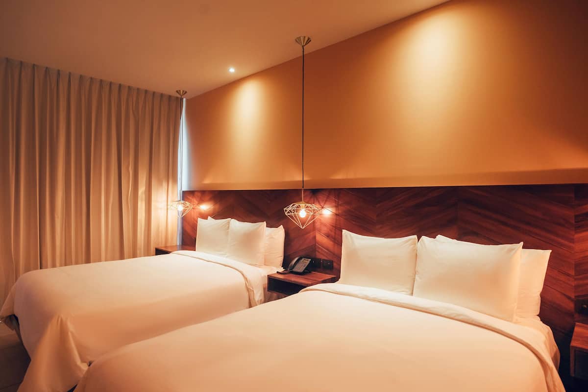 A hotel room with two beds, a wooden headboard, a nightstand with a phone, and a hanging light fixture.