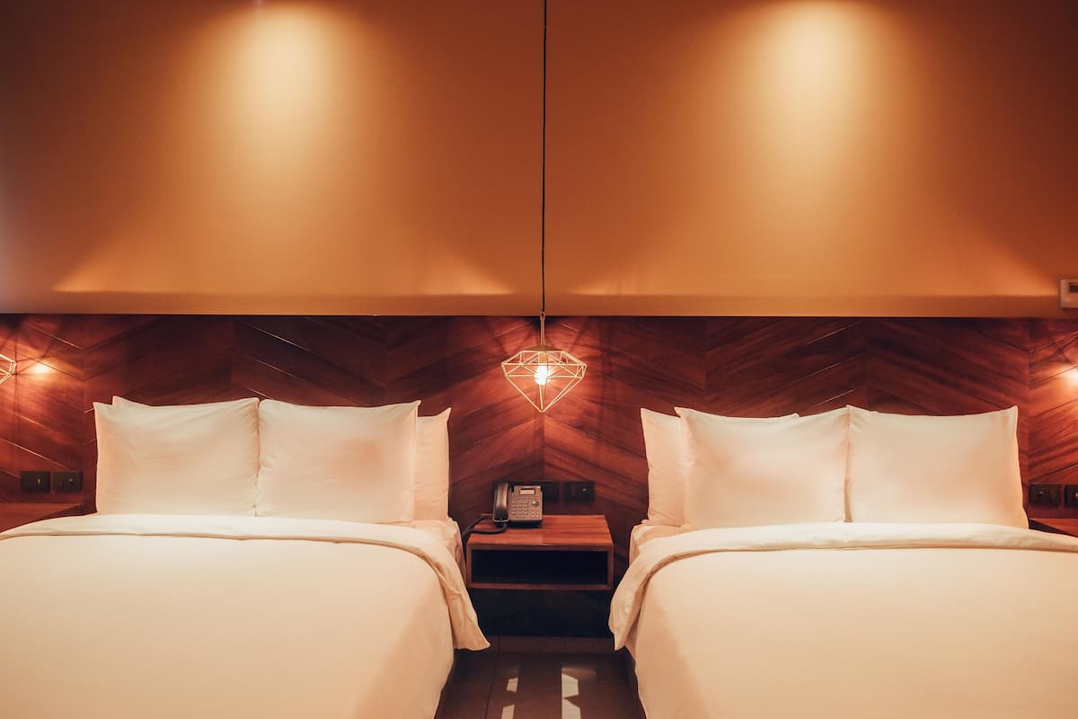 A hotel room with two beds, a wooden ceiling, and a small bedside table with a phone.