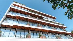 Een hotel met meerdere verdiepingen, balkons, grote ramen en potplanten.