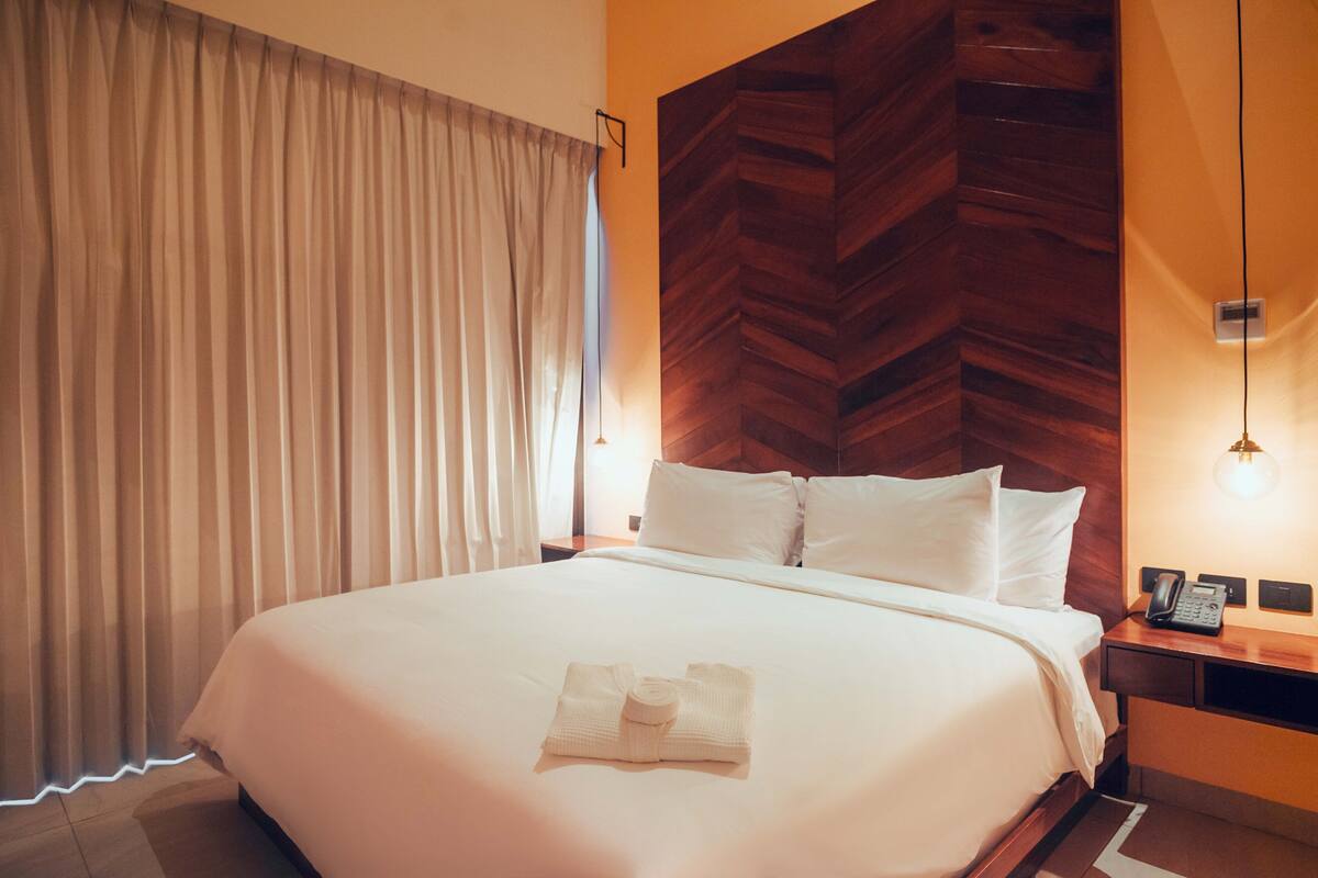 A hotel room with a large bed, a wooden headboard, a bedside table with a lamp, and a telephone.