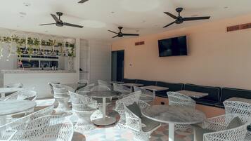 Un restaurante con mobiliario de mimbre blanco, ventiladores de techo y un televisor en la pared.